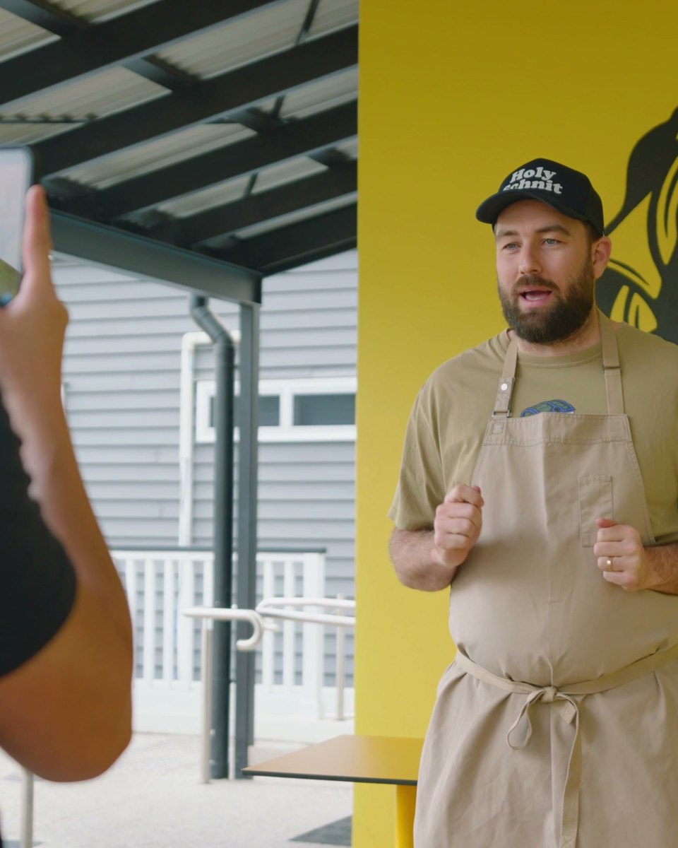 A creator filming Sunny Side Sandwiches owner Mack in front of the shop's mascot wall