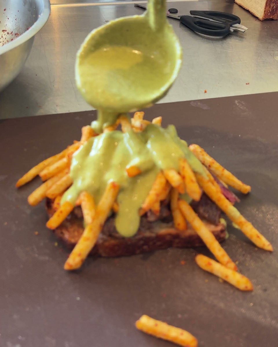 Green sauce poured over the steak and fries sando at Sunny Side Sandwiches